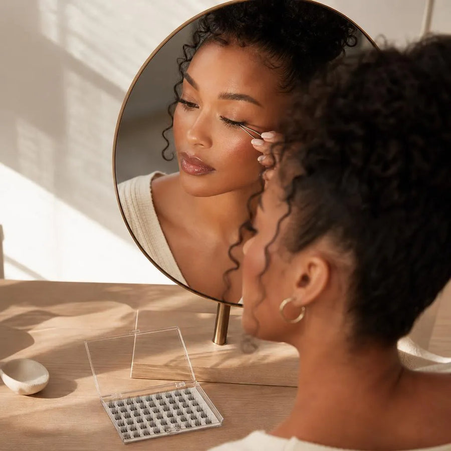 Woman applying lash clusters at a vanity mirror